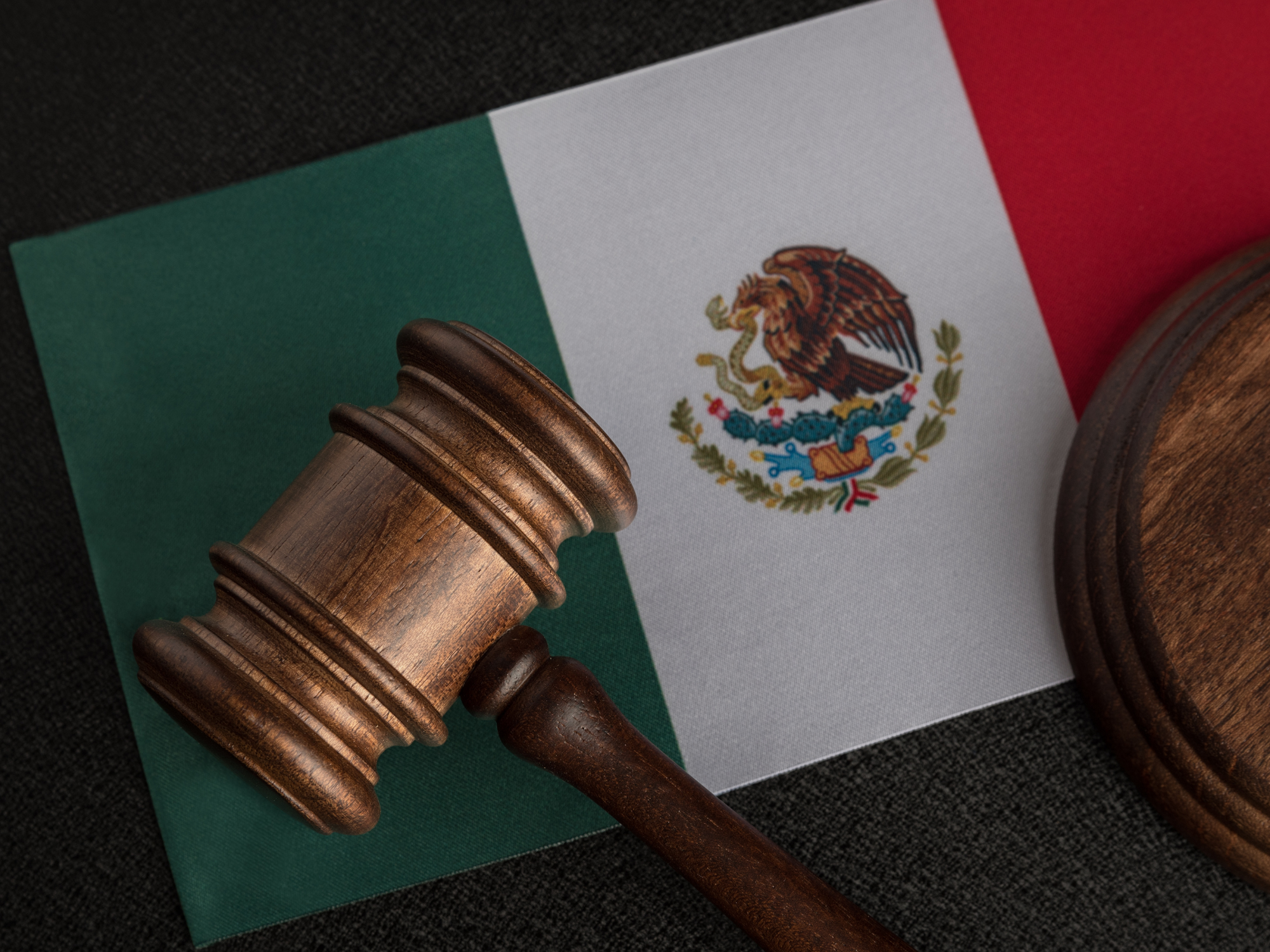 A wooden judge's gavel rests on a Mexican flag, symbolising law and justice in Mexico.