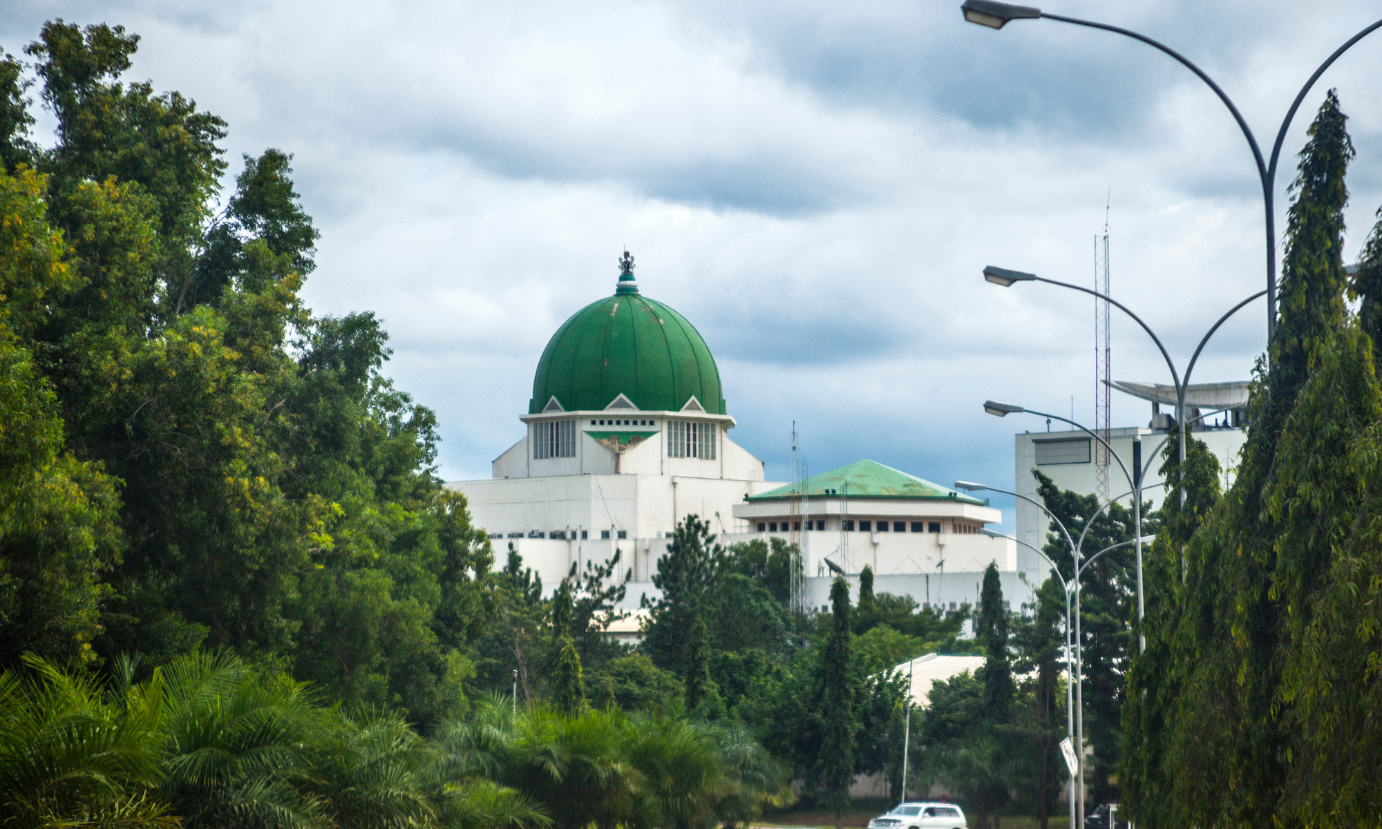 Green and white government building at the end of a road lined with green trees.