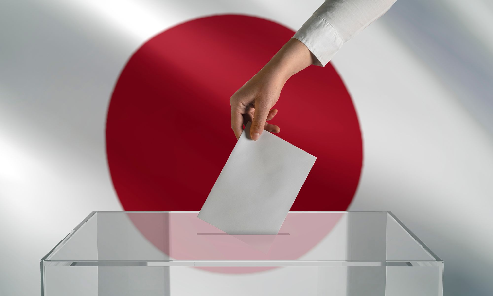 A hand is putting a white voter slip into a ballot box in front of the Japanese flag.