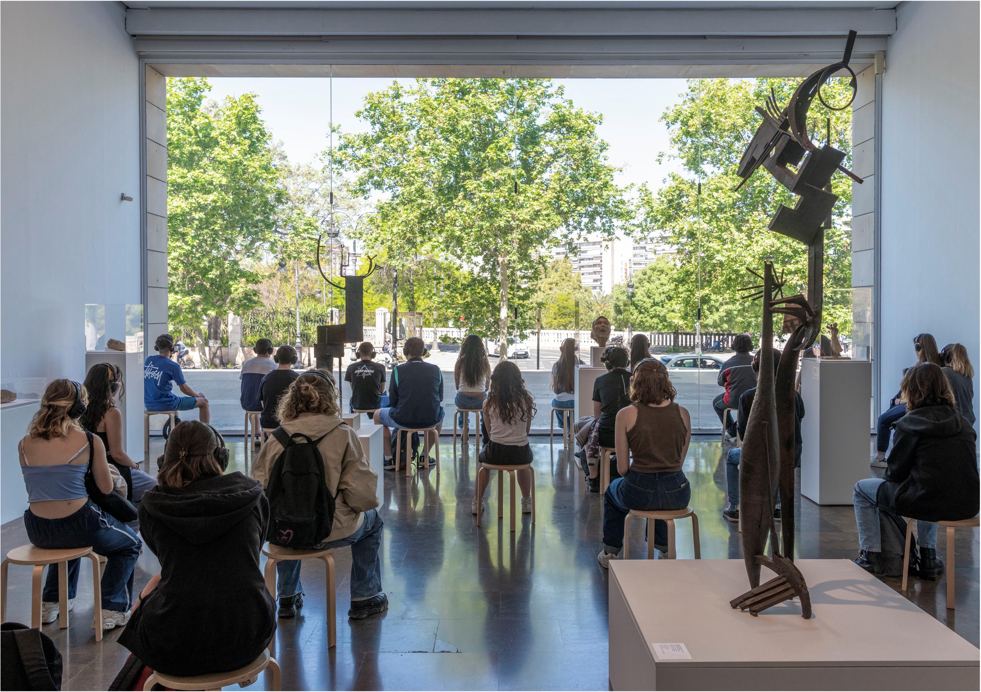 A group of people sat on chairs spaced out in a museum, looking out a window.