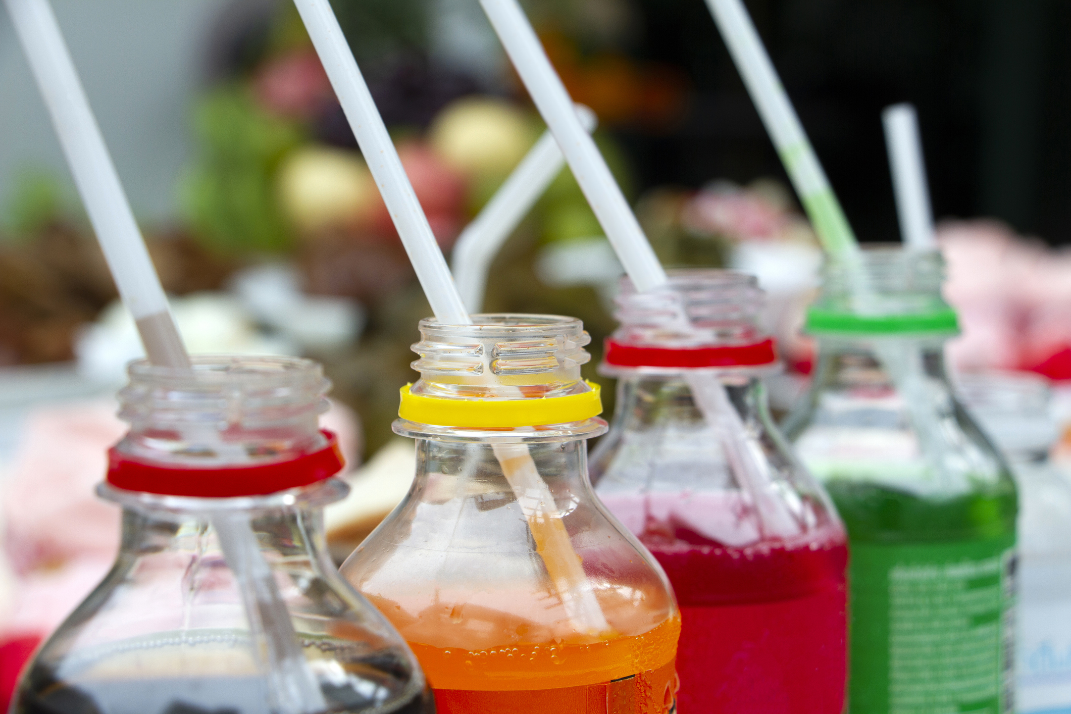 A row of coloured drinks in plastic bottles, straws in each