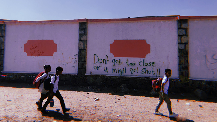 Children walk past a graffitied wall in Aden, Yemen. The graffiti reads 'Don't get too close or u might get shot!!'.