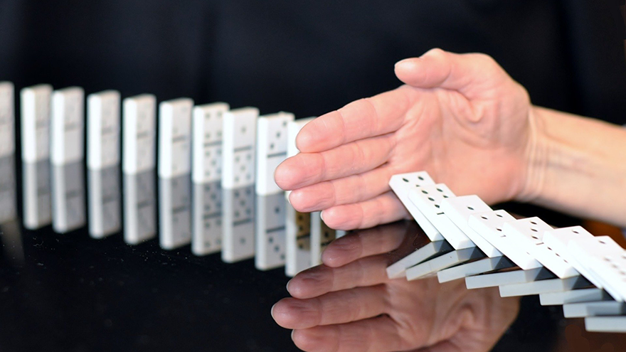 Hand stopping dominoes falling