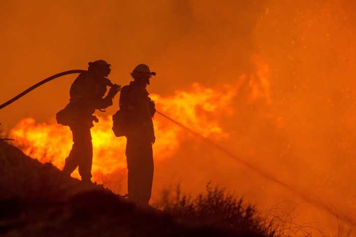 Photo of silhouette of two firefighters against a backdrop of fire