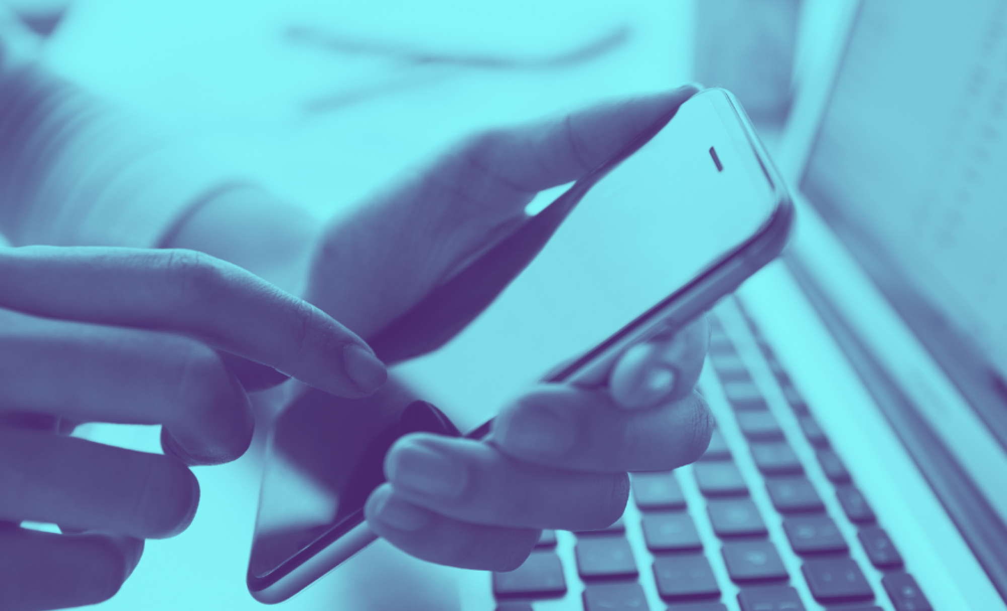 Close-up on hands holding smartphone above computer keyboard