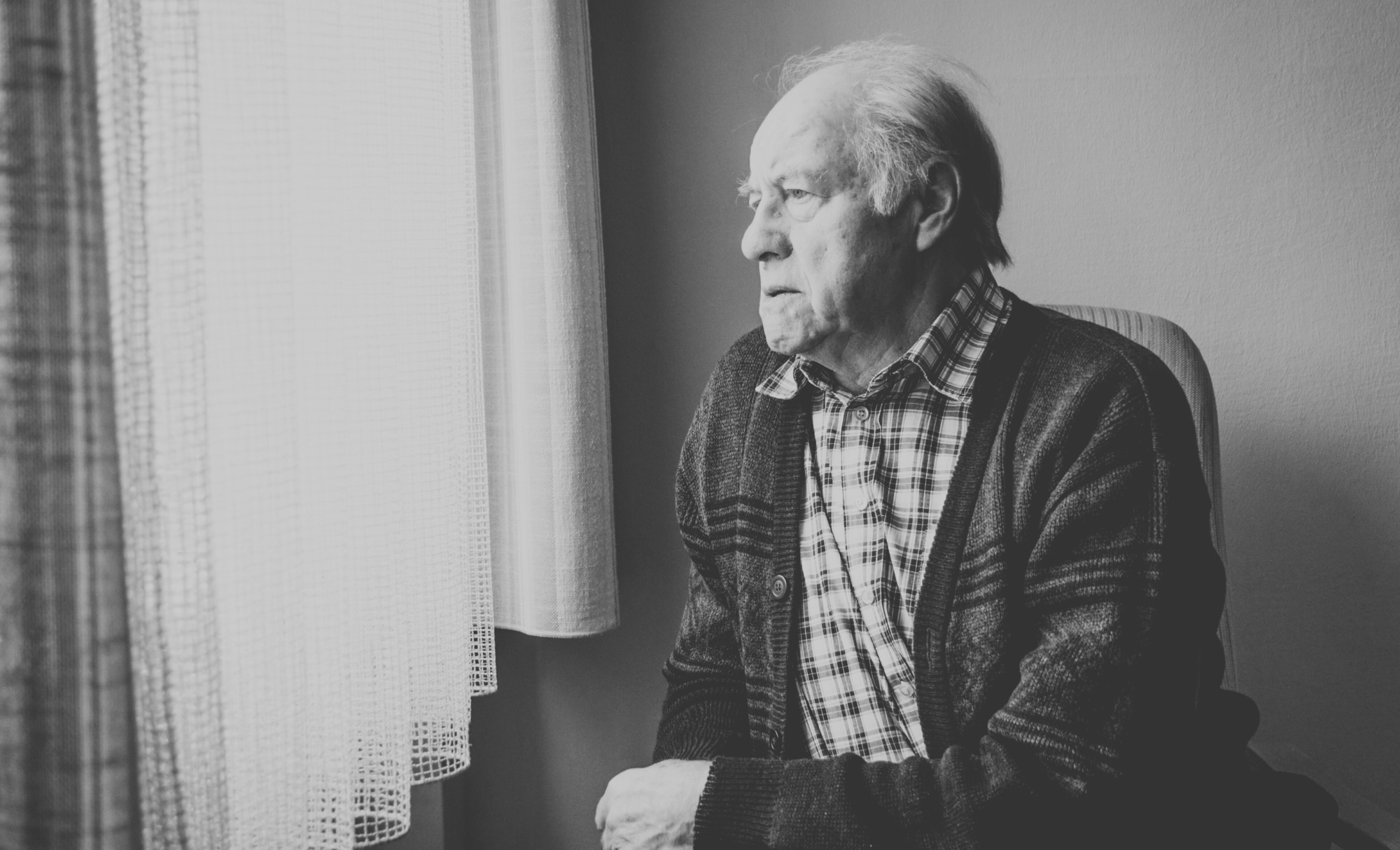An older man stares out of a window looking melancholy