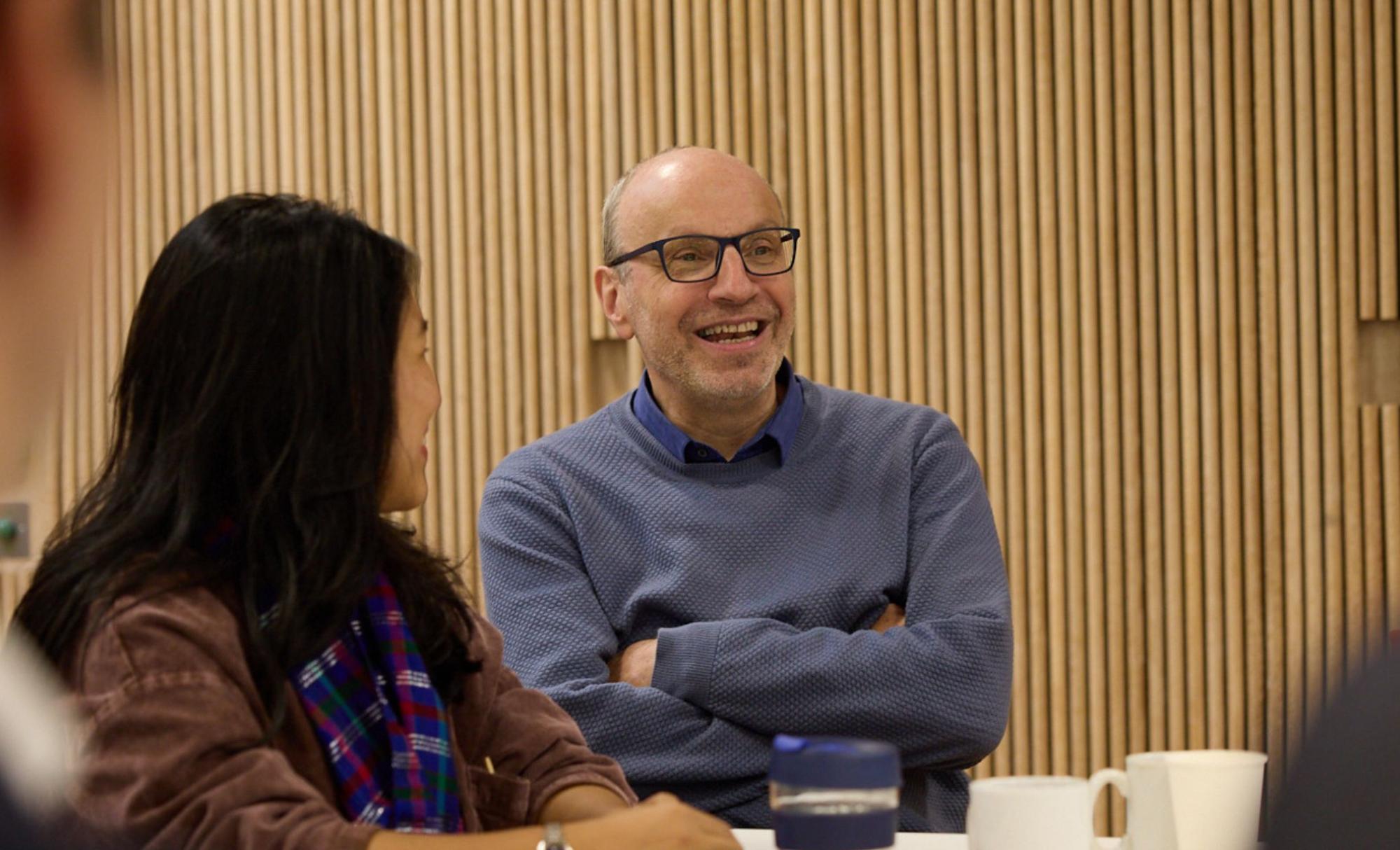 Professor Stefan Dercon sits at a table during induction next to two women. They are all smiling.