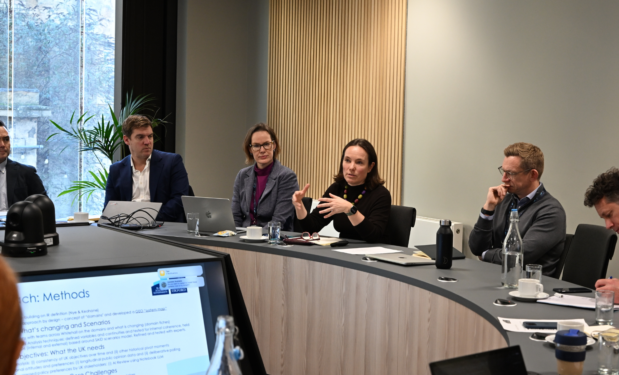 Jenny Bates sits centre with people either side, she is addressing a round table