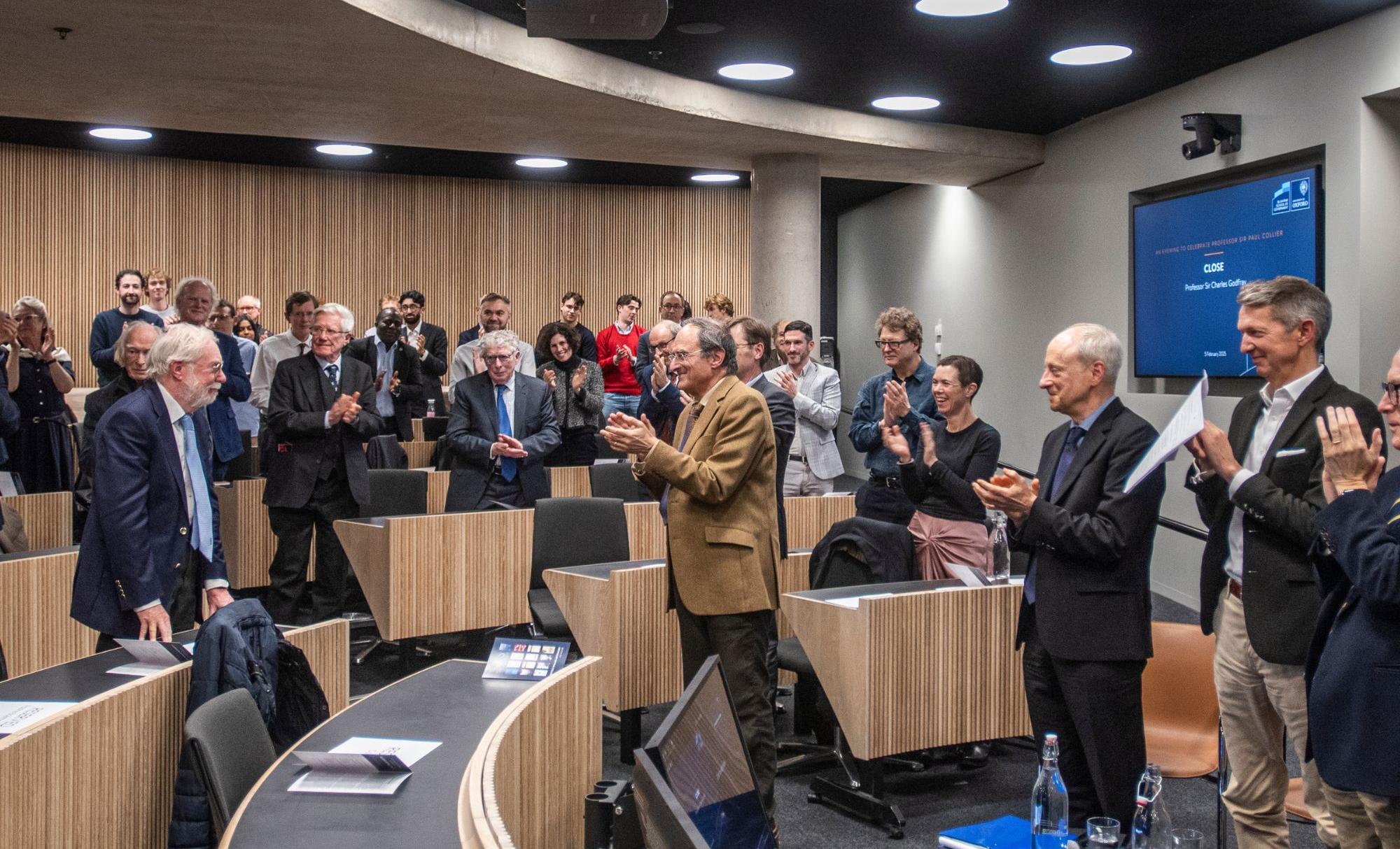 Paul Collier stands as everyone claps around him in a lecture theatre