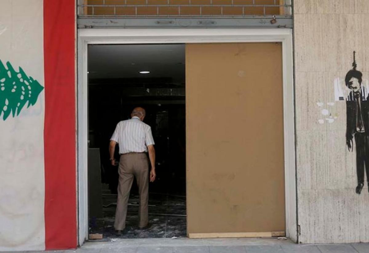 A man walks into his store completely shattered by the blast. On the wall to his left, hangs a flag of Lebanon and on the wall to his right, is a painted image of a hanged politician. Credit: Marwan Tahtah.