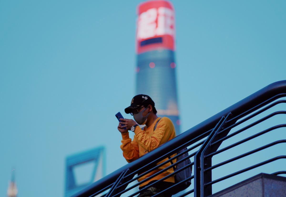 A man with mask looks at his phone on a bridge in Shanghai