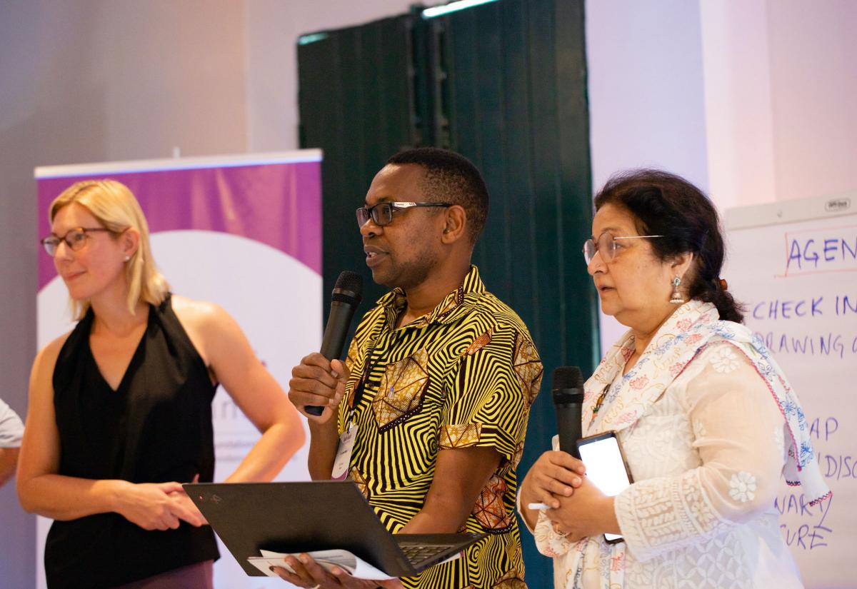 Man presents with a laptop and microphone. Women stand either side.