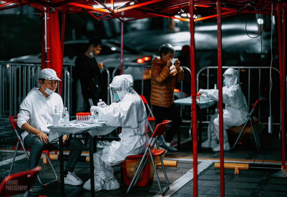 In China, under a red temporary structure with neon lighting, people are carrying out COVID-19 tests.