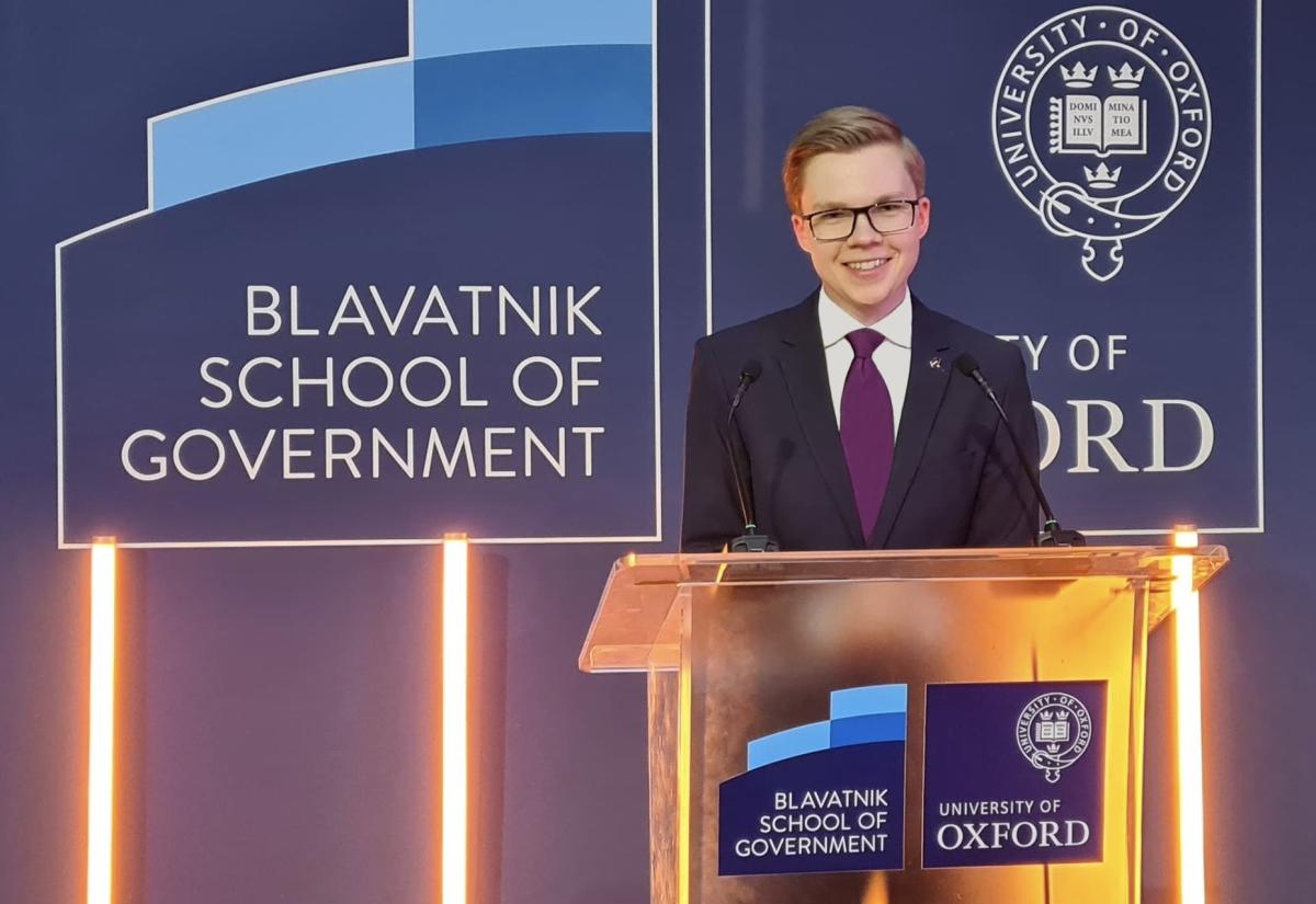 Picture of Arnolds Eizensmits smiling behind a podium with a blue background and the logo for the Blavatnik School of Government