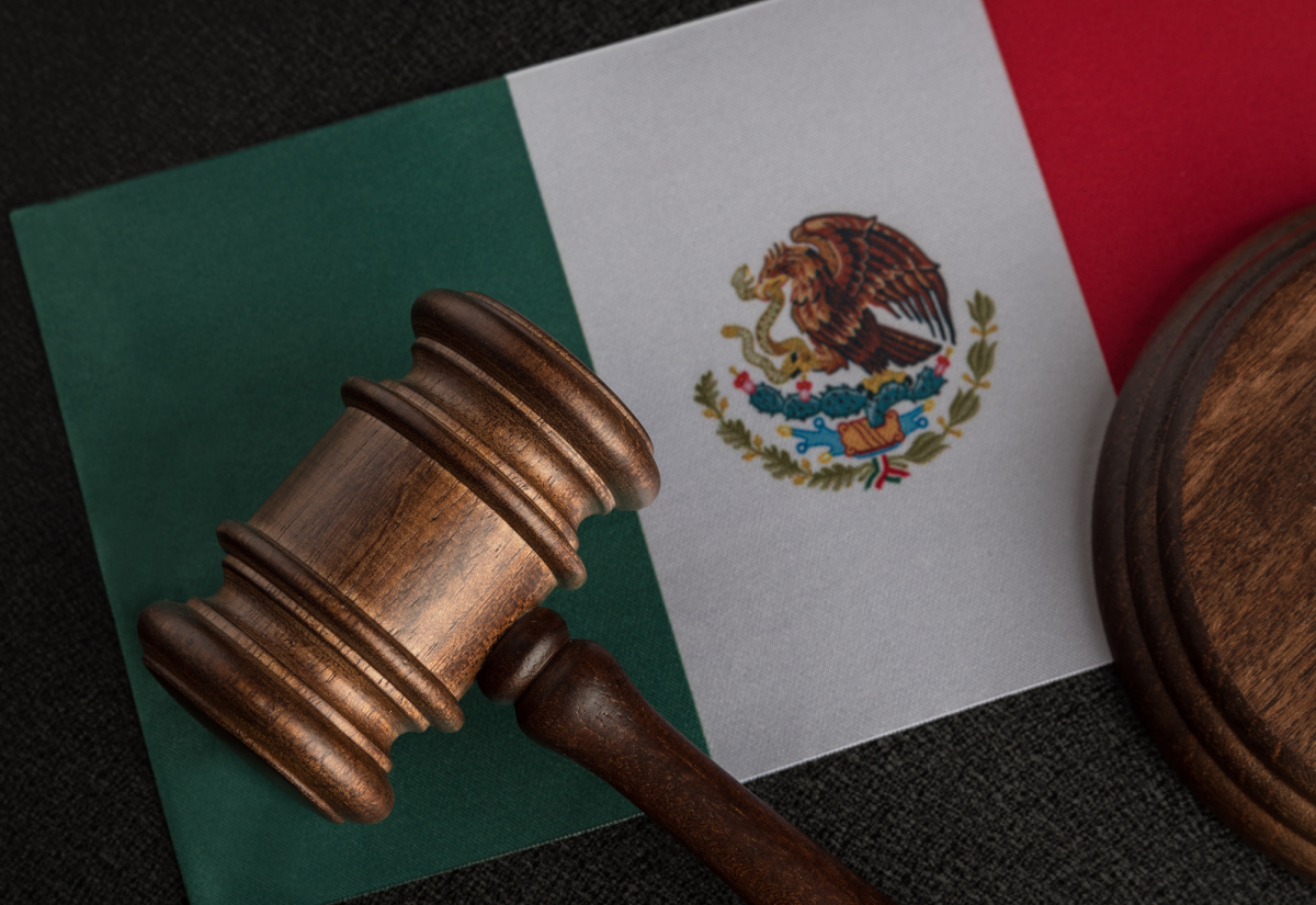 A wooden judge's gavel rests on a Mexican flag, symbolising law and justice in Mexico.