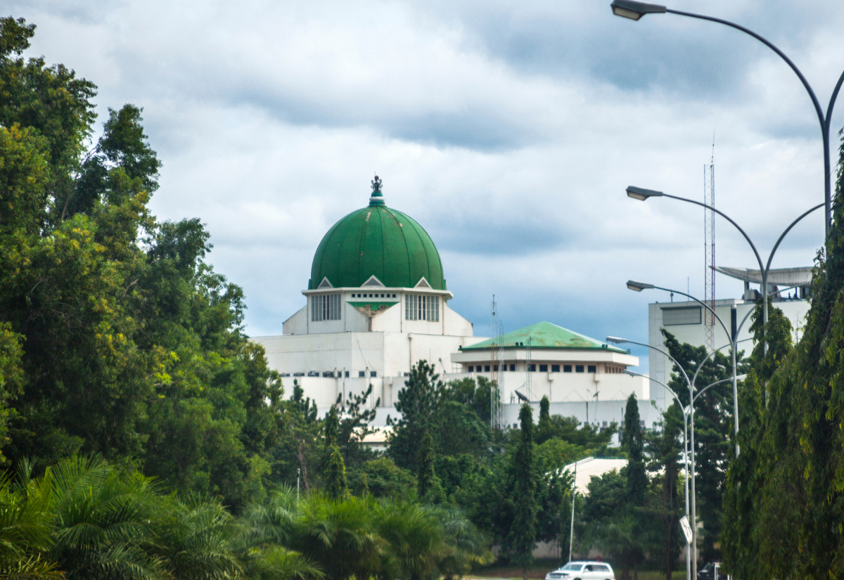 Green and white government building at the end of a road lined with green trees.
