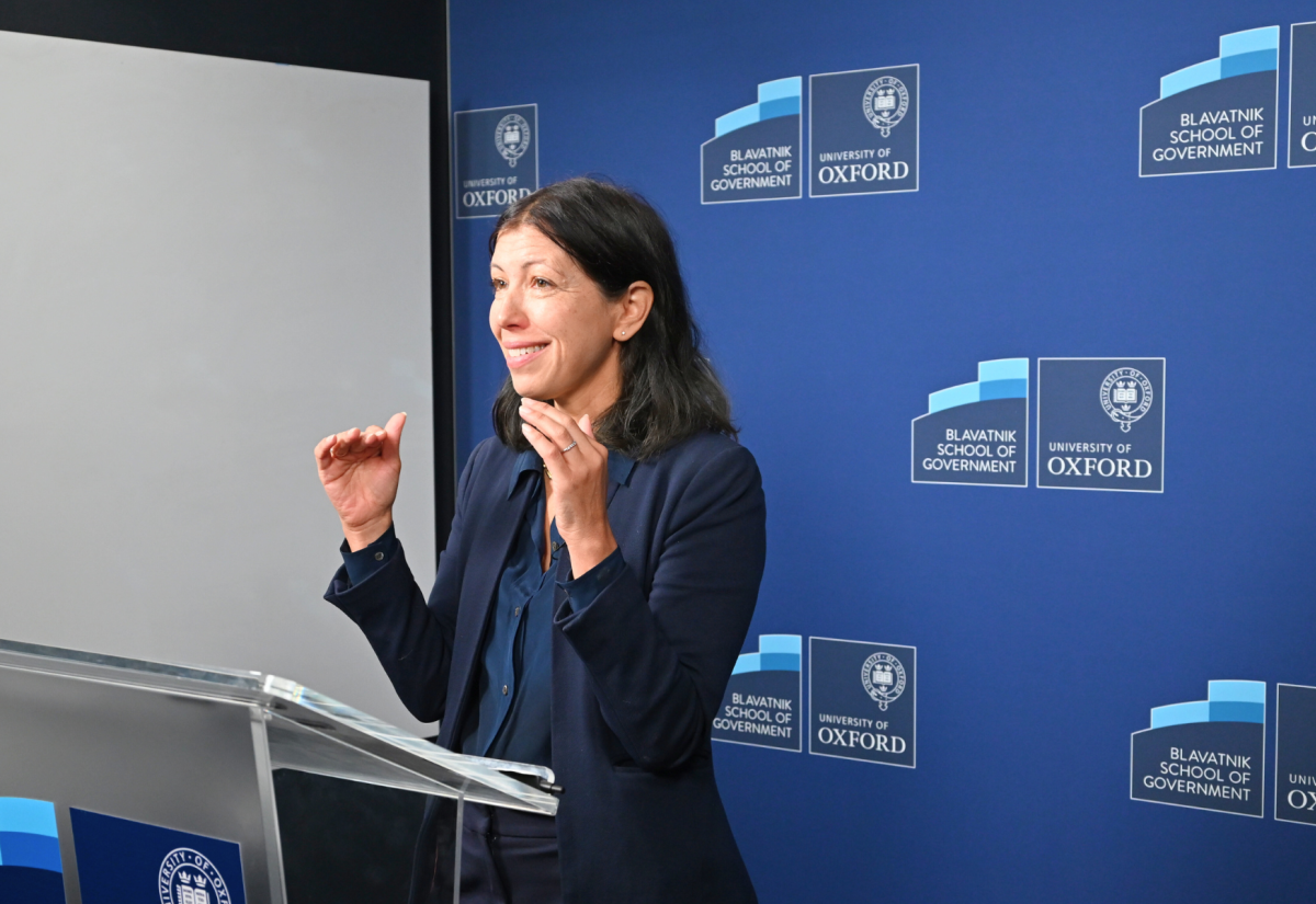 Professor Maya Tudor stands at a lecturn teaching in a green room with a branded Blavatnik School backdrop.