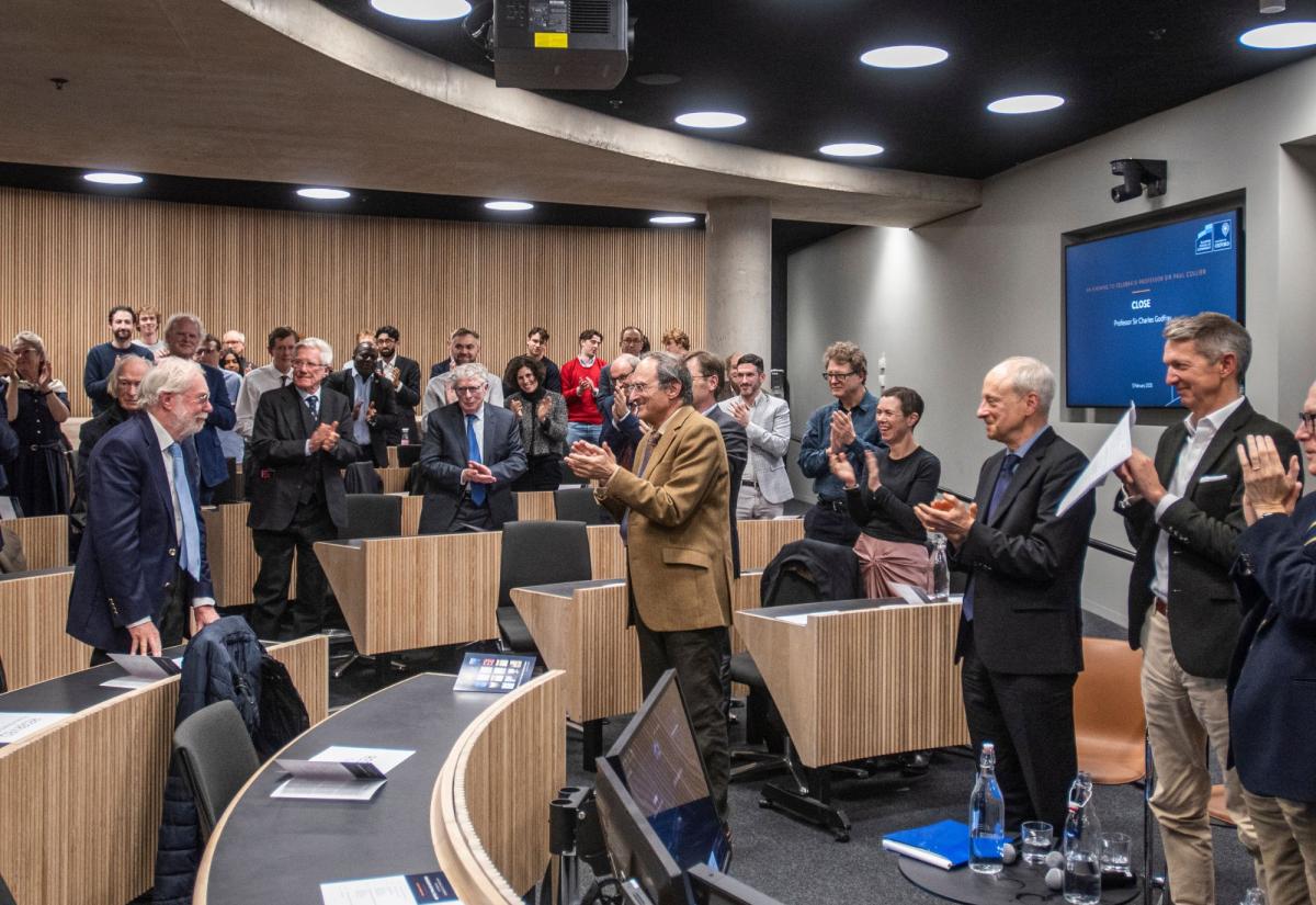 Paul Collier stands as everyone claps around him in a lecture theatre