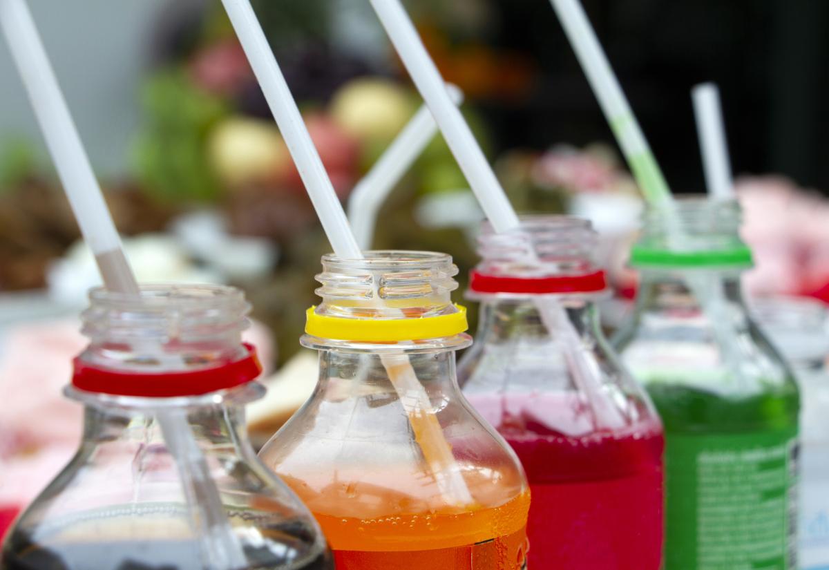 A row of coloured drinks in plastic bottles, straws in each
