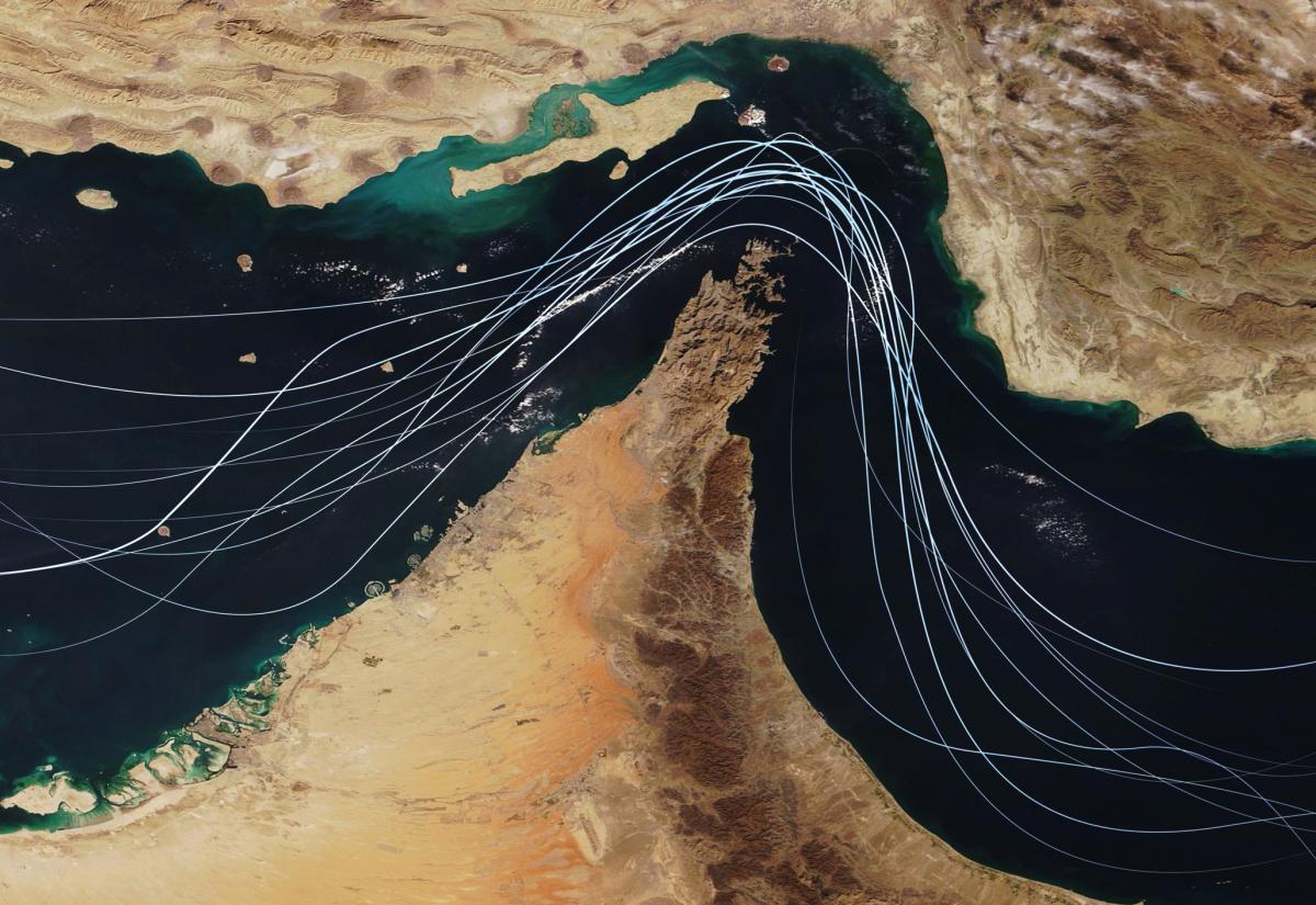 Satellite view of the Strait of Hormuz with white graphic lines representing global shipping lanes and maritime traffic between the Persian Gulf and Gulf of Oman. 