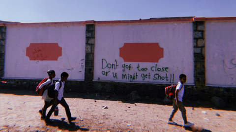 Children walk past a graffitied wall in Aden, Yemen. The graffiti reads 'Don't get too close or u might get shot!!'.