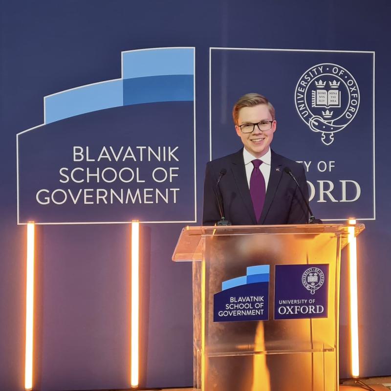 Picture of Arnolds Eizensmits smiling behind a podium with a blue background and the logo for the Blavatnik School of Government
