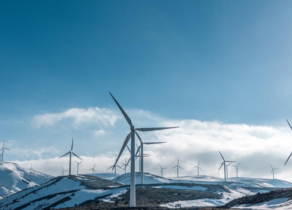 Wind turbines across a snowy hillside - photo by Jason Blackeye for Unsplash